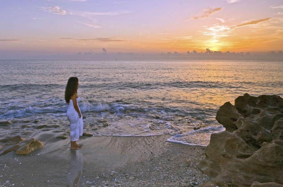 lovely hispanic lady in white dress watches sunrise at the beach;