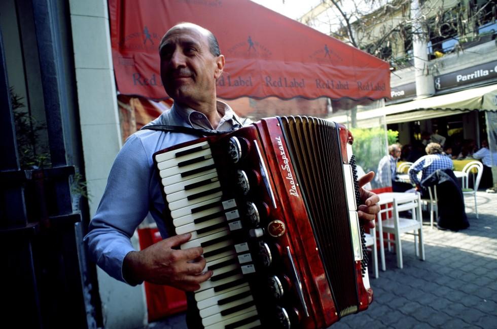 person; cityscape; urban; scene; Mercado del Puerto Montevideo, Uruguay, accordion, face, fingers, folklore, hand, instrument, man, music, musical, musician, people, performer, play, red, performance, outside, outdoors, town, city; Mercado del Puerto Monte