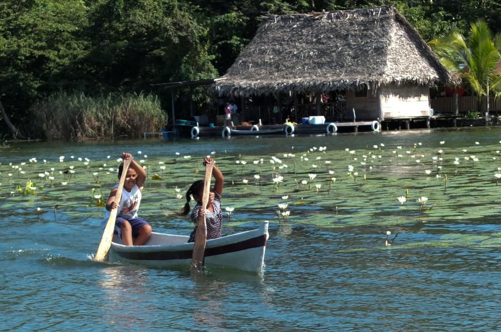 RIO DULCE, GUATEMALA -  DECEMBER 6: Children are rowing in a small boat near white lilies,at the arrival of tourists to sell them home made presents on December 6, 2013, in Rio Dulce, Guatemala.