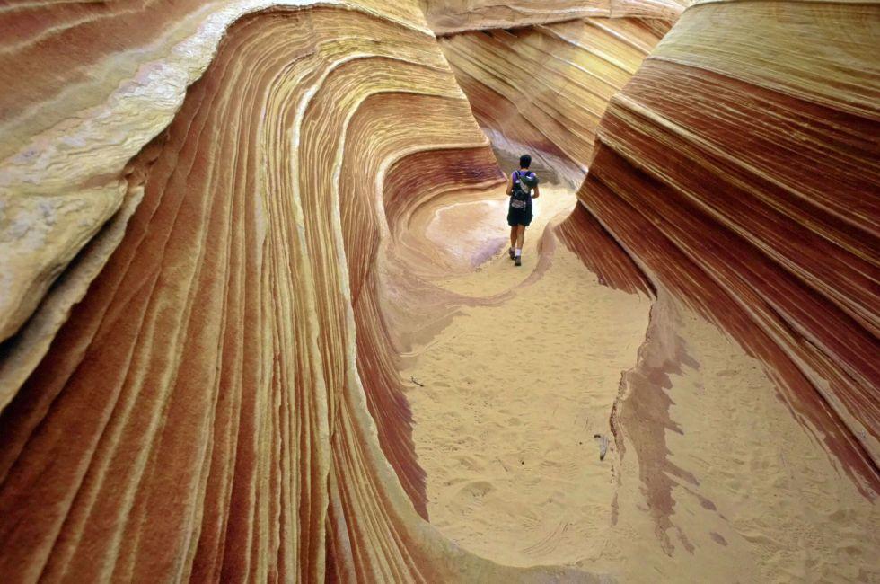 A lone hiker explores the astonishing candy stiped sandstone hidden amongst the geologic folds of the Colorado Plateau, Paria, Arizona