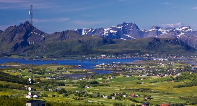 Scenic panorama with green meadows, town of Leknes and snowy peaks of picturesque Lofoten islands in Norway; 